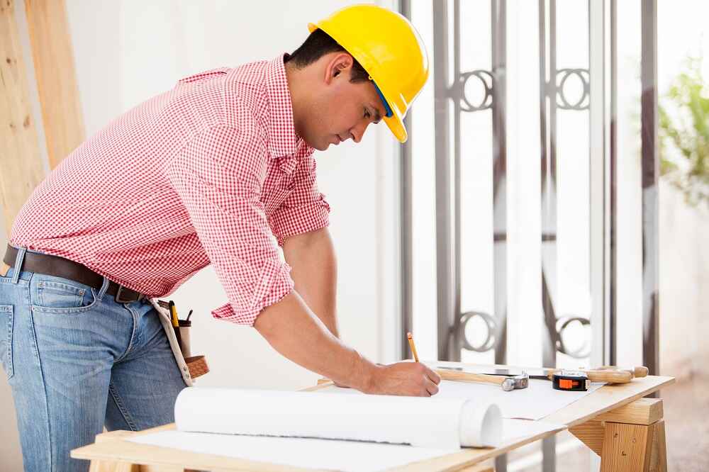 Worker in a hard hat drawing plans on a worktable